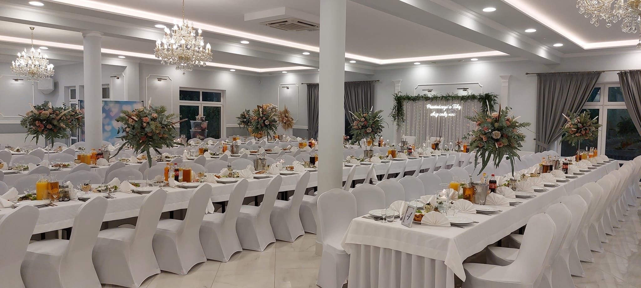 Sala Glamour Chroboty - sala weselna z dekoracjami kwiatowymi w odcieniach pomarańczu i pudrowego różu, podświetlana scena pary młodej