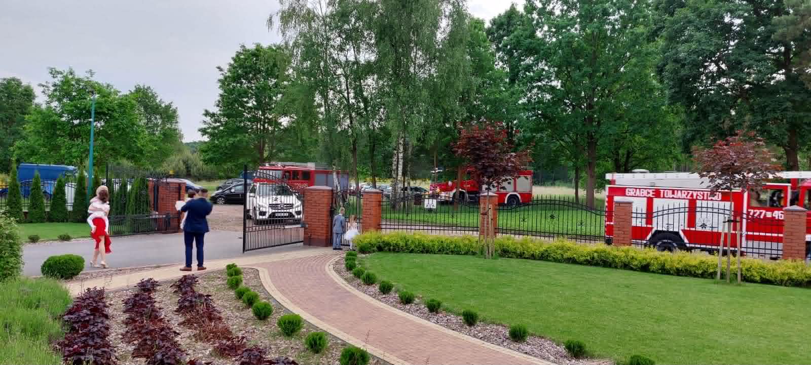 Sala Glamour pod Żyrardowem - zadbany ogród i brama wjazdowa latem, powitanie pary młodej przez wozy strażackie OSP, zieleń i formowane krzewy