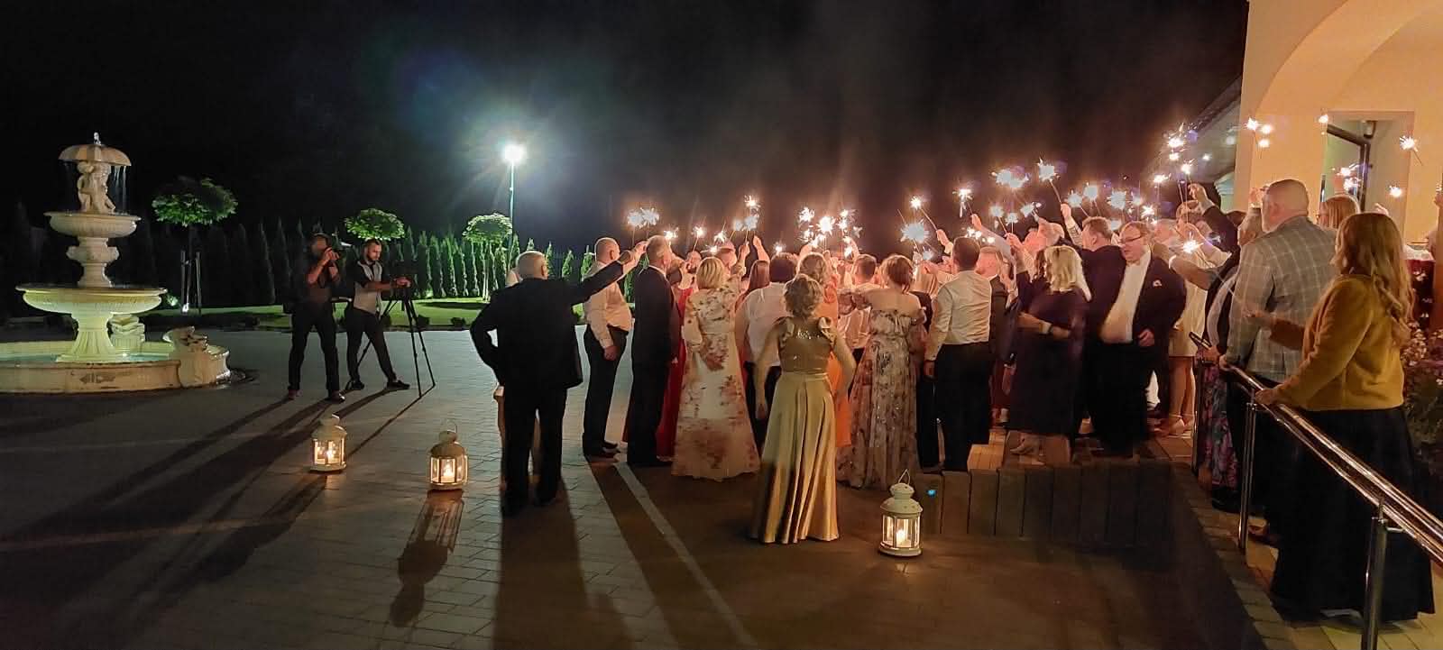 Sala Weselna Glamour pod Żyrardowem - goście z zimnymi ogniami przed salą nocą, podświetlona fontanna i lampiony, wieczorna atmosfera wesela